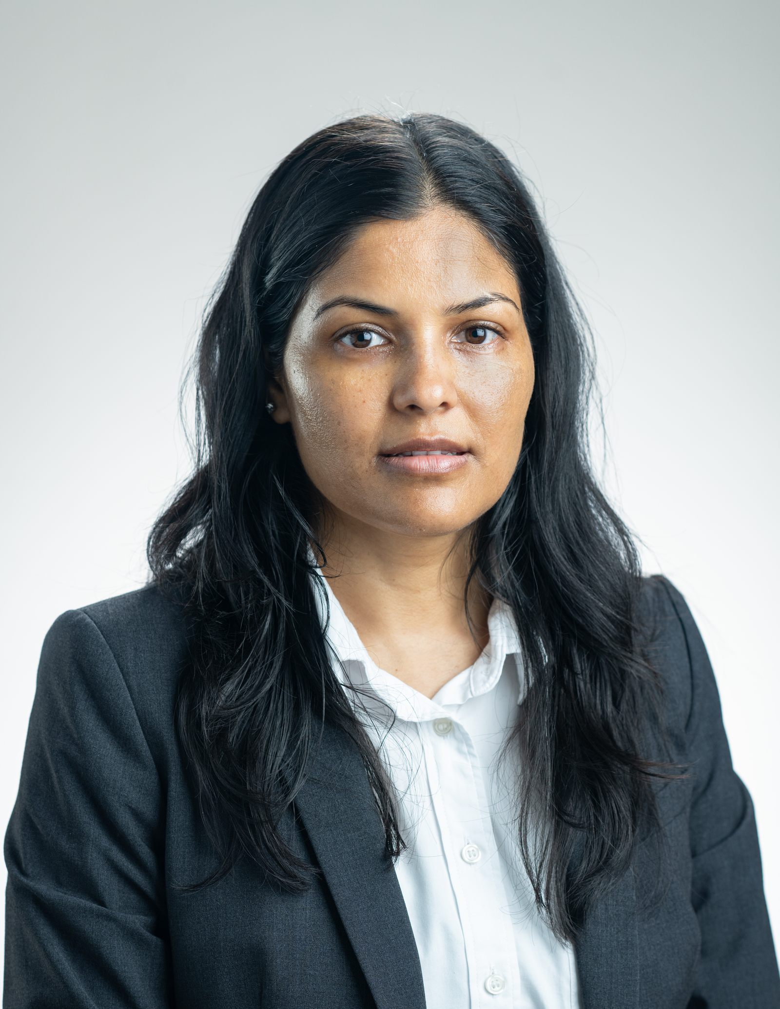 Headshot of a woman with long black hair, wearing a white collared shirt and a black blazer.