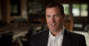 A man in a dark jacket and white shirt sits in a chair