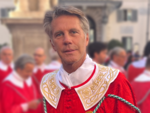 A man with grey hair wears a red top