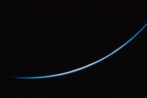 The edge of Earth is a thin line curving upward from left to right. The line is different shades of blue.