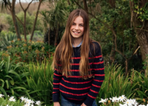 Princess Charlotte wears a blue and red striped jumper and stands in a field of daisies