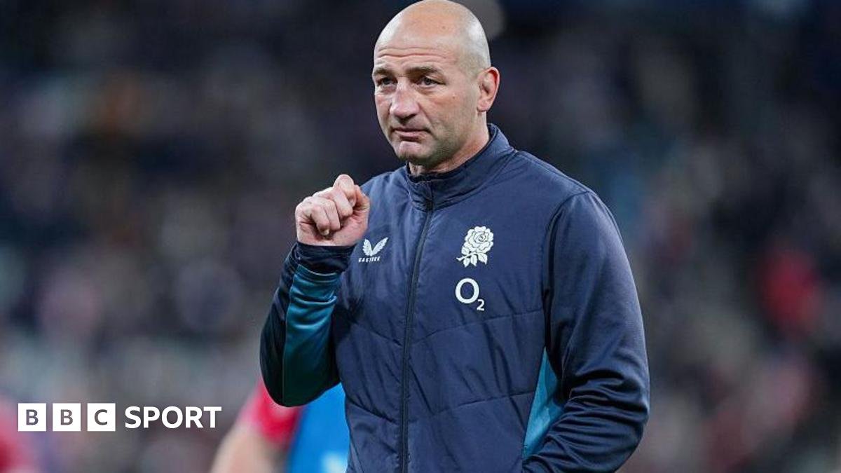 Steve Borthwick, wearing a nany blue zip-up England jacket, looks into the distance, his right hand raised to shoulder level