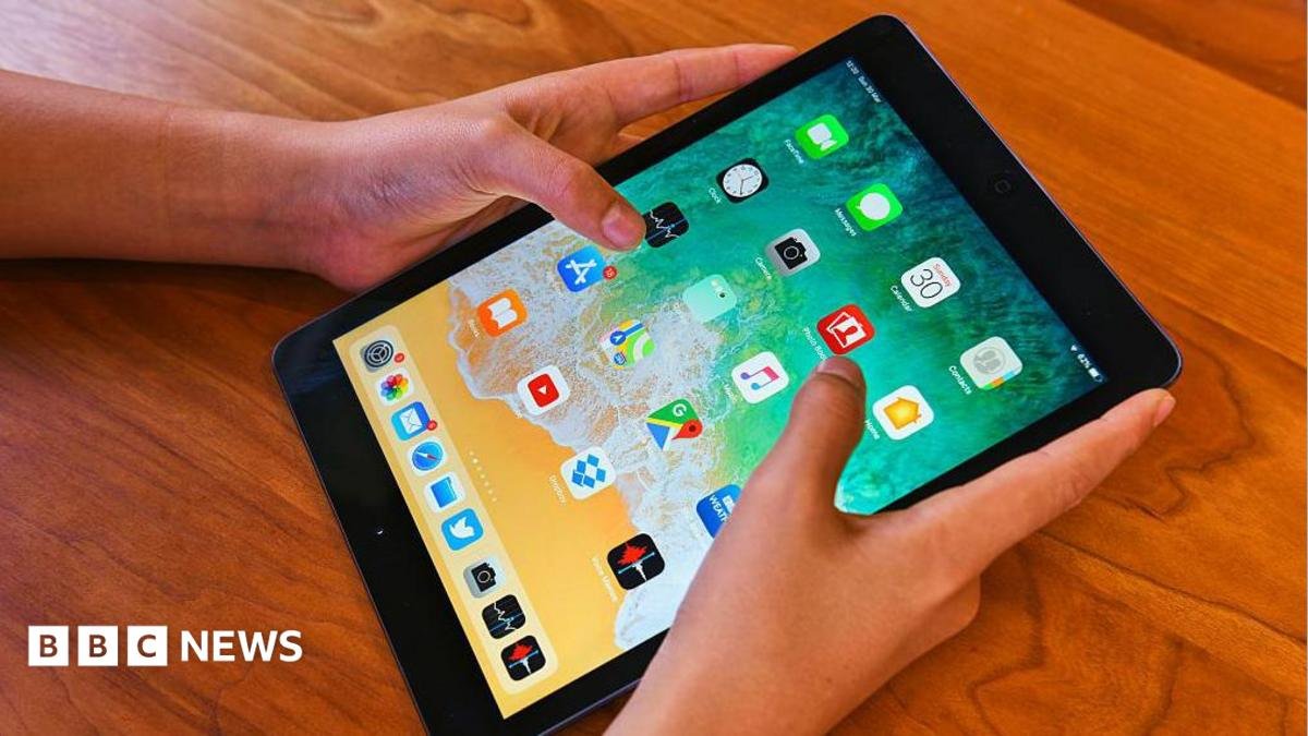 Person's hands holding an iPad on a table.