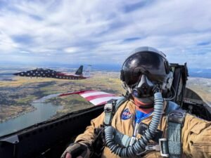 A photographer takes a selfie from the rear seat of a jet aircraft during flight, with another jet visible through the window.