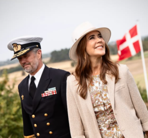 King Frederik and Queen Mary smile as they walk in front of a Danish flag