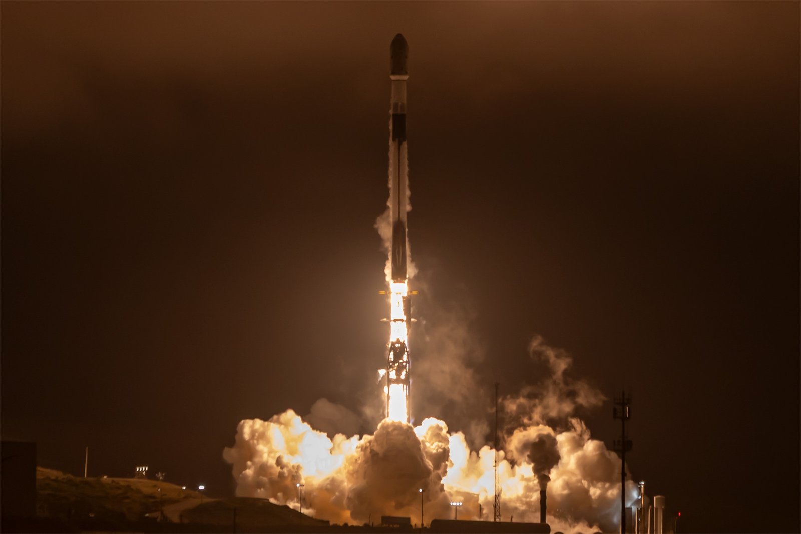 Image shows a night sky with the ignition of a white rocket launching vertically.