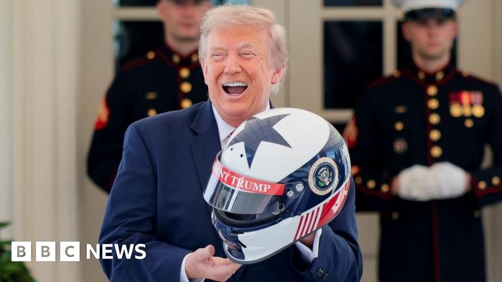 President Trump holds a red, white and blue race car helmet while wearing a blue suit
