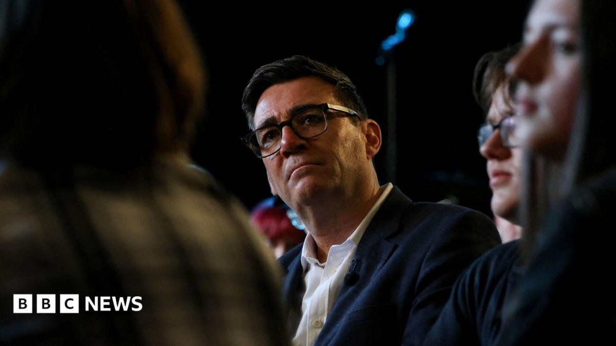 Andy Burnham. He has dark hair, wearing glasses, a navy blazer and white shirt.