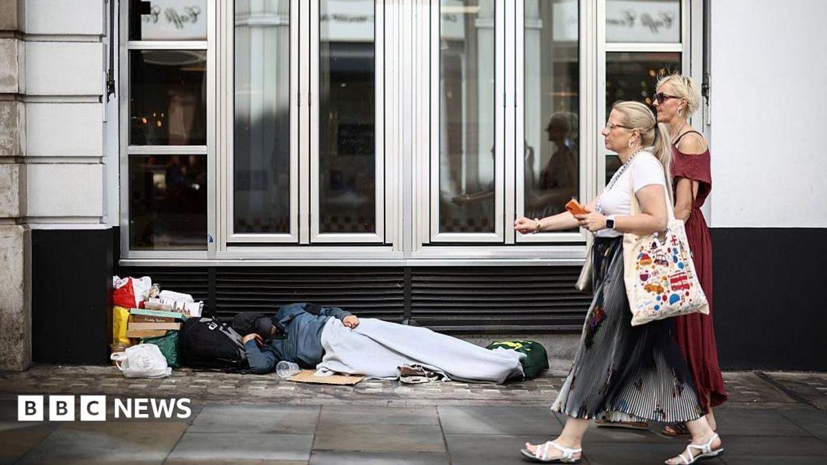 Two women walk past a person lying on the pavement in London, 28 July