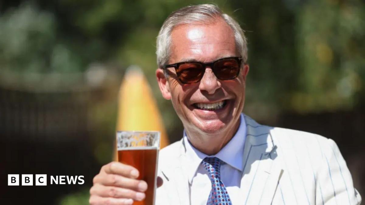 Nigel Farage wearing sunglasses and holding a pint of beer. He is smiling.