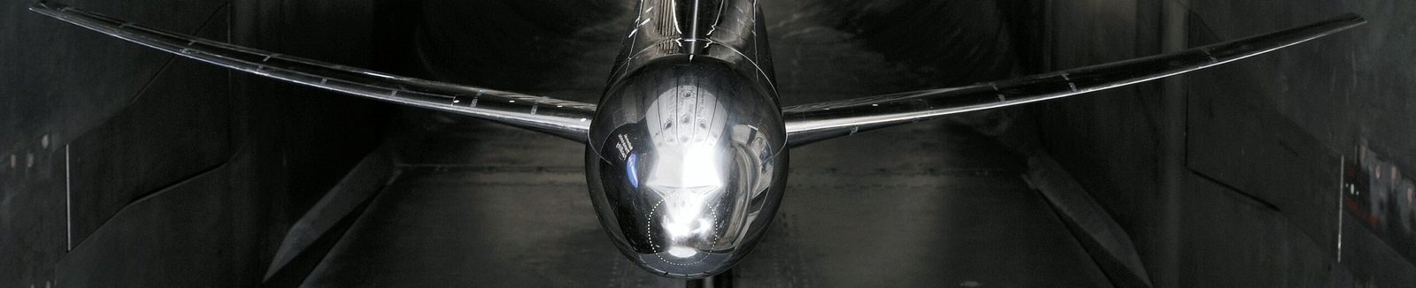 A metallic CRM aircraft model with swept wings is positioned inside a dark wind tunnel.