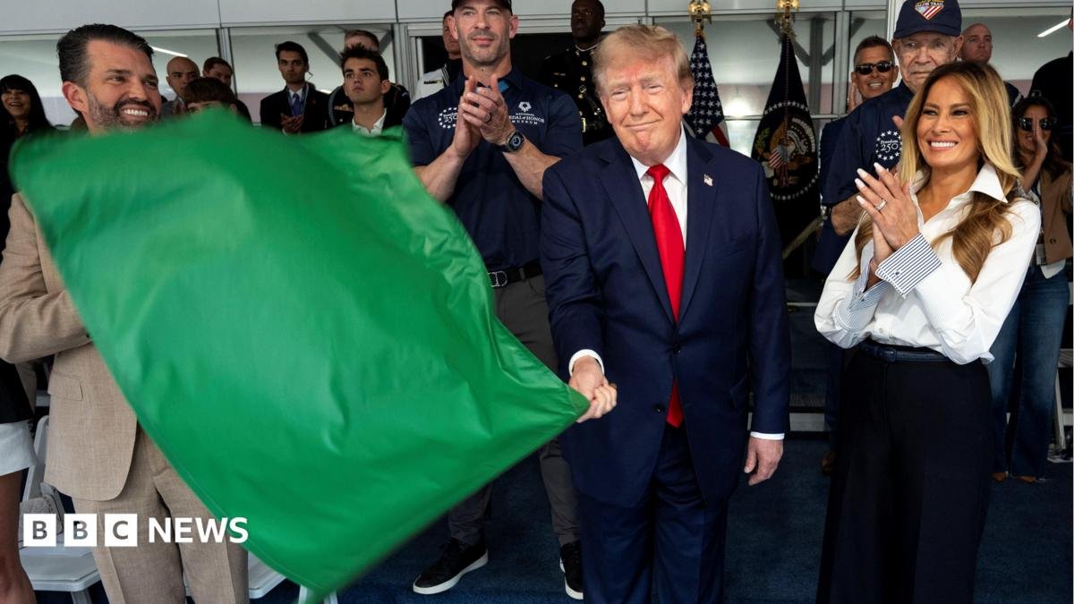 Donald Trump waves a green flag as he stands next to his wife Melania who is smiling and clapping