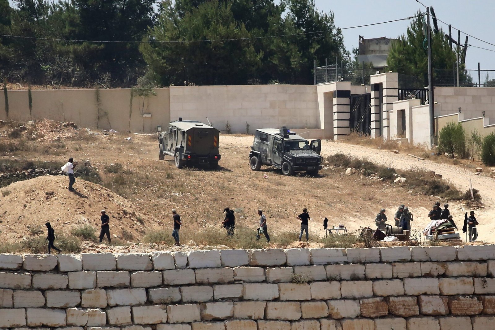 Israeli soldiers stand guard next to settlers in front of Palestinian homes that they have blockaded in the village of Qusra, south of Nablus, in the occupied West Bank, Wednesday, Aug. 12, 2026.