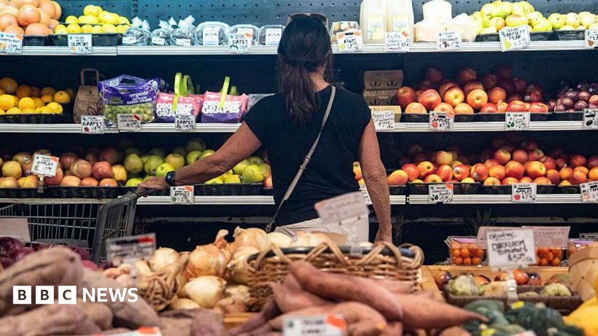 A woman looks at apples in a supermaket aisle.