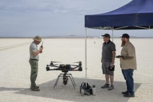 One man communicates with a hand-held radio, as two other men wait to the side for the go-ahead command to fly an experiment on a drone.