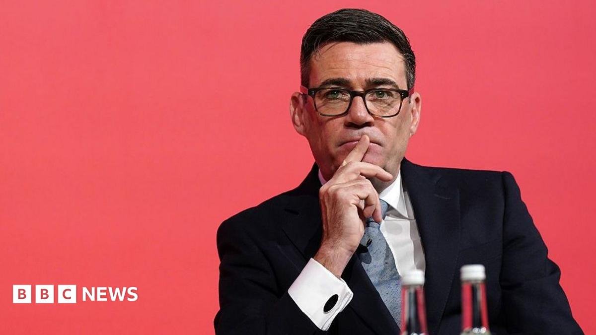 Andy Burnham looks pensive while sitting down with a red background.